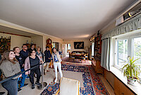 Eine Frau führt eine Gruppe Menschen durch das Wohnzimmer Adenauers