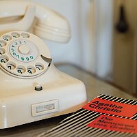 Ein Nachttisch neben einem Bett mit Telefonapparat und einem Taschenbuch-Krimi