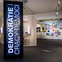 Ausstellungsraum mit großem Display mit der Aufschrift "Demokratie"