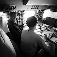 Zwei Personen sitzen in einem Flugzeug und arbeiten an einem Tisch