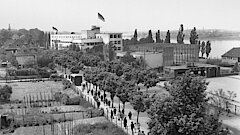 Pädagogische_Akademie_1949 Schwarzweißfotografie der ehemaligen Pädagogischen Akademie am Bonner Rheinufer. Auf dem Dach weht eine Deutschlandflagge, vor dem Gebäude flanieren zahlreiche Menschen.