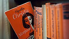 Eine Reihe in einem Bücherregal mit Kriminalromanen. Ein Taschenbuch von Agatha Christi ist halb herausgezogen.
