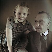 Konrad Adenauer sitzt auf einem Sessel, den Arm auf der Lehne. Hinter ihm steht seine Tochter Libet im Alter von etwa 10 Jahren