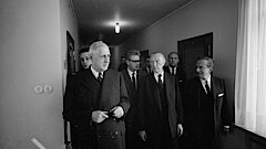 Konrad Adenauer und Charles de Gaulle laufen, gefolgt von anderen Männern, durch einen Flur