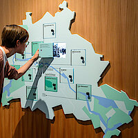 Eine Frau betrachtet eine Videoinstallation, die in einer Landkarte an einer Ausstellungswand integriert ist