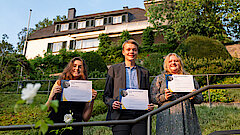 Zwei Schülerinnen und ein Schüler stehen im Garten vor dem Wohnhaus von Konrad Adenauer.