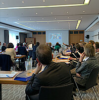 Teilnehmer blicken im Konferenzraum auf eine Leinwand