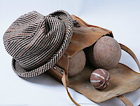 Ein karierter grau-brauner Pepita-Hut und eine Ledertasche mit Boccia-Kugeln