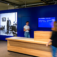 Zwei Frauen am Counter der Ausstellung, Holztheke und blaue Wand, Großfoto zeigt Adenauer am Schreibtisch